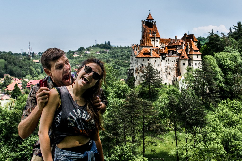 A photo of Brett pretending to be Dracula and Bianca posing with a fake blood bite outside of Bran Castle in Romania. This castle is famously known as Dracula's Castle, and visitors can have fun pretending to be the legendary vampire while exploring its halls and corridors.