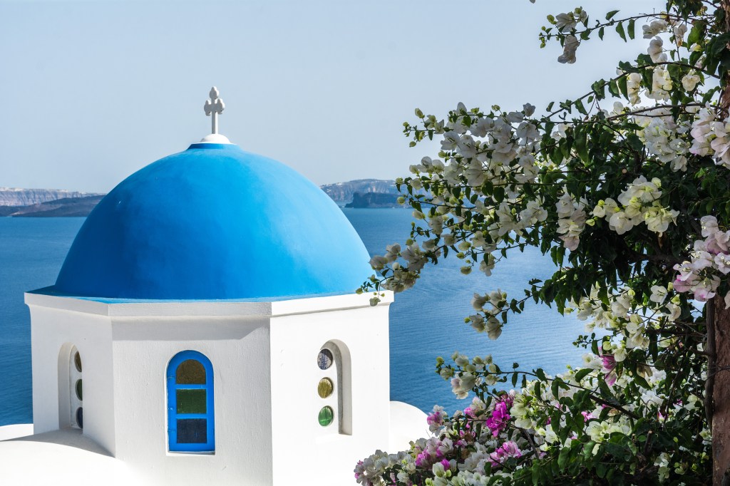The traditional blue top roof and white buildings of Santorini in Greece. Experience the beauty of Santorini with our travel blog.