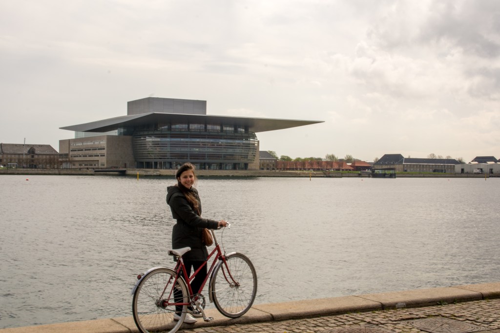 View of a cyclist riding through the streets of Copenhagen, Denmark - renting a bike is the perfect way to explore more of the city in a shorter amount of time. Don't miss out on discovering hidden gems while enjoying the picturesque waterfront.