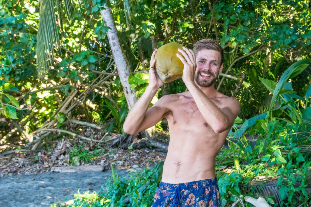 Brett Cutting a Coconut for Food and Drink' - Immerse yourself in the tropical experience as Brett skillfully opens a coconut, providing fresh food and drink. Discover the art of survival and indulgence in paradise.