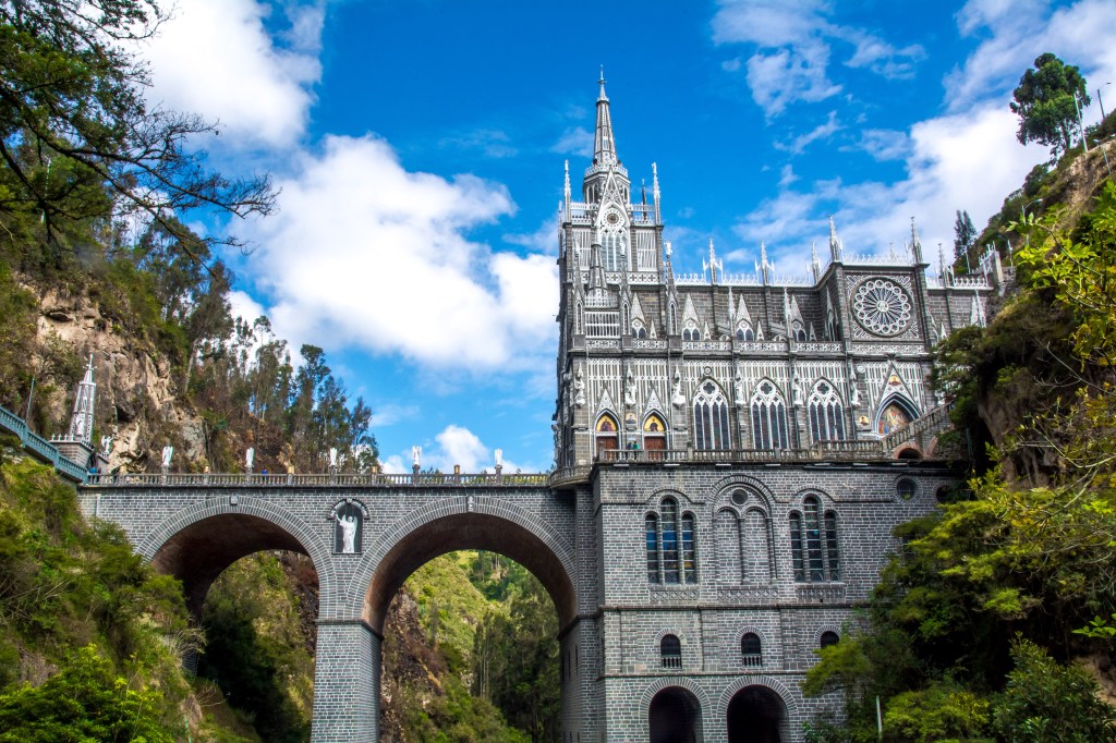 Las Lajas Sanctuary, an architectural marvel, standing dramatically across a stunning cascading bridge, surrounded by lush natural beauty. This iconic Colombian religious site combines breathtaking aesthetics and tranquil nature, making it a must-visit attraction.