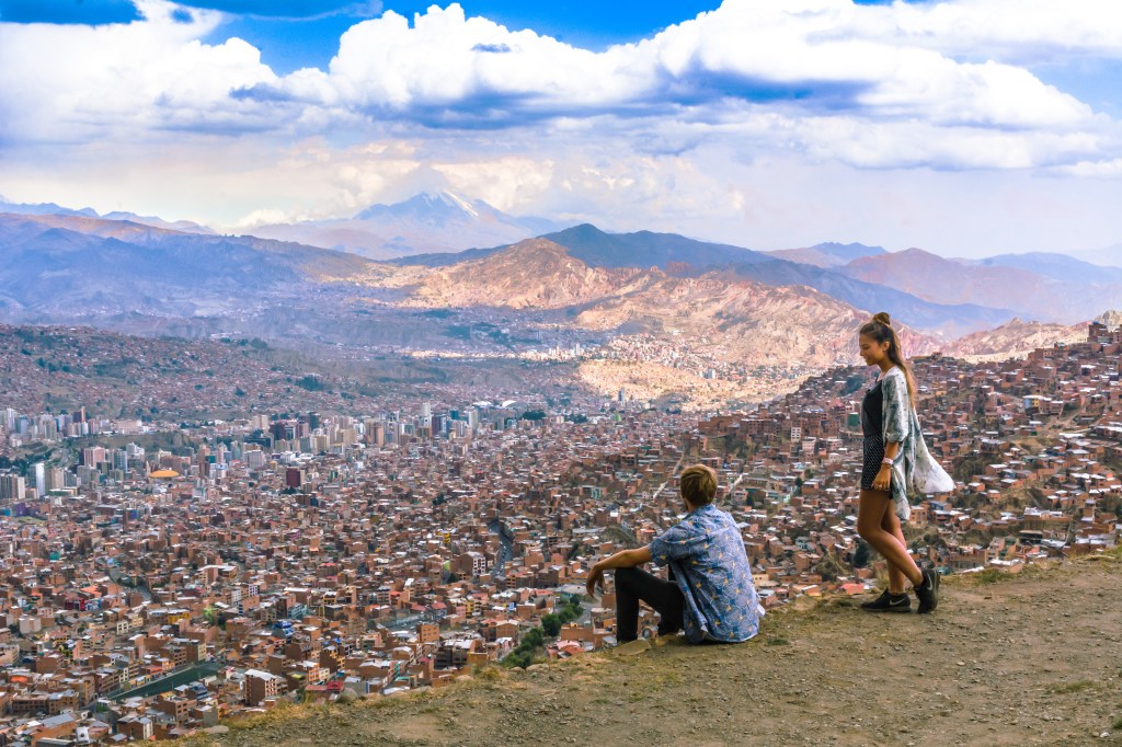 Image capturing Bianca and Brett admiring the panoramic view of the bustling cityscape of La Paz, Bolivia, showcasing the vibrant urban life and scenic beauty from an elevated viewpoint.