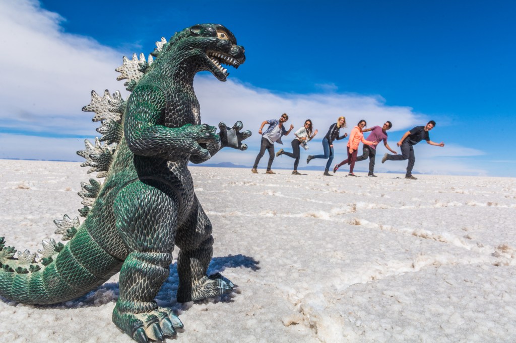 Image capturing Bianca and Brett joyfully posing with toy dinosaurs amid the surreal landscapes of Bolivia's Salt Flats, adding a playful touch to the adventure and beauty of this iconic travel spot