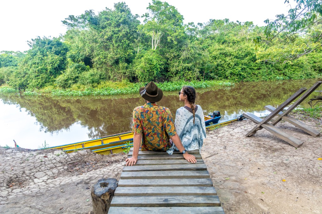 Image capturing Bianca and Brett seated near the Amazon River, eagerly anticipating wildlife sightings, showcasing the thrill of exploring the diverse fauna of the Amazon rainforest.