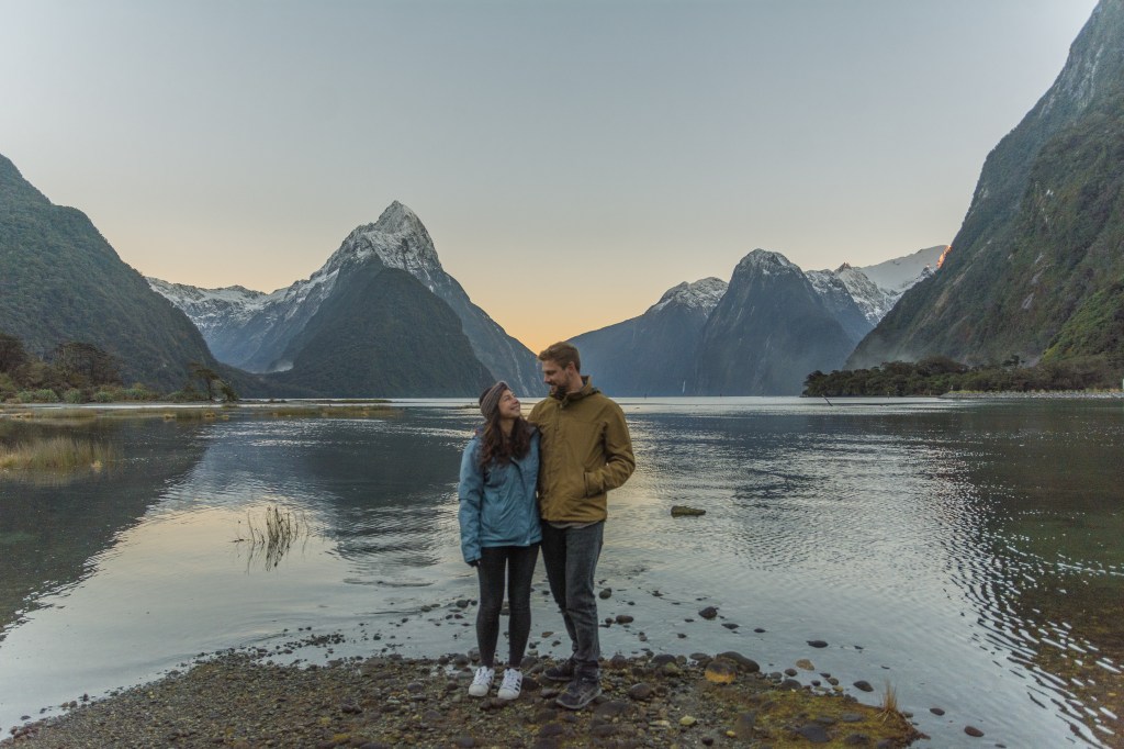 Spectacular sunset moment: Bianca and Brett capturing the beauty of Milford Sound. Immerse yourself in the magical hues of the sunset at this iconic New Zealand destination.