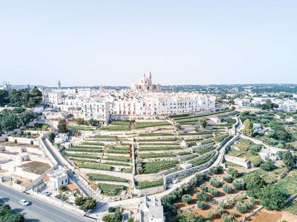 Drone shot of Locorotondo, a charming Italian village known for its whitewashed houses and winding streets, showcasing the beauty of the historic town set against the lush green countryside.