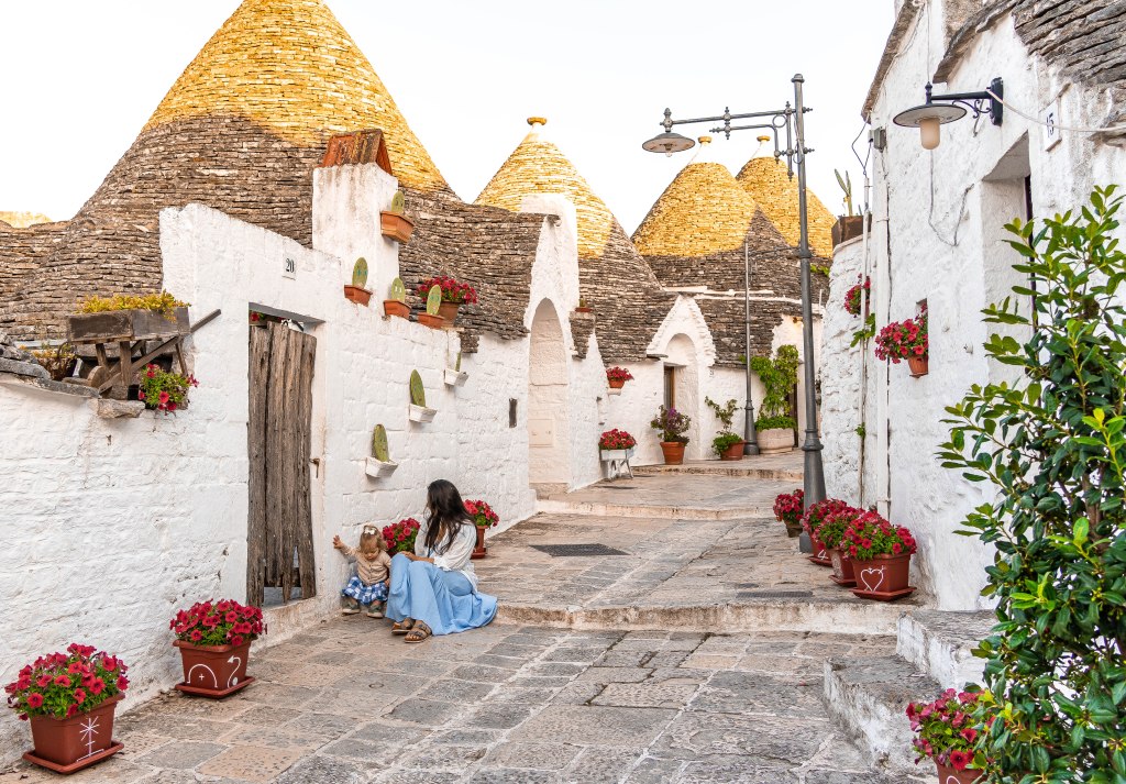 Image of a person taking a seat on the cobbled streets of Alberobello, Italy, surrounded by the unique trulli houses, a UNESCO World Heritage site, offering a glimpse into the charming traditional architecture of the region.