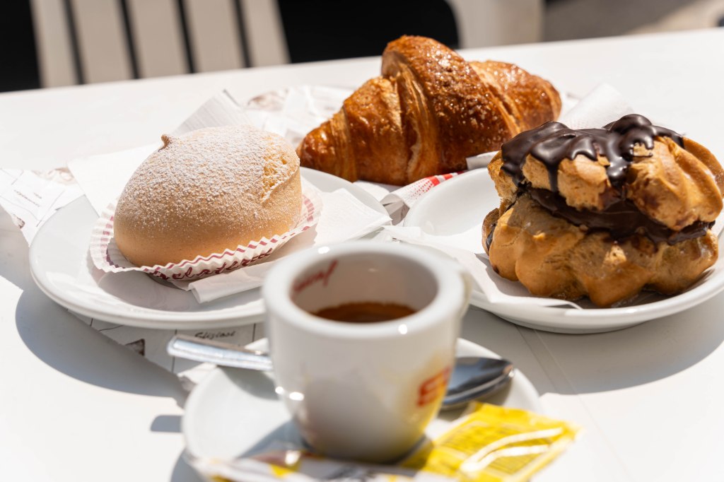 Image of bakery treats including nun's breasts (tette della monache), croissant, chocolate eclair, and espresso, enjoyed at a local bakery, offering a delicious taste of Italian pastries and coffee culture.