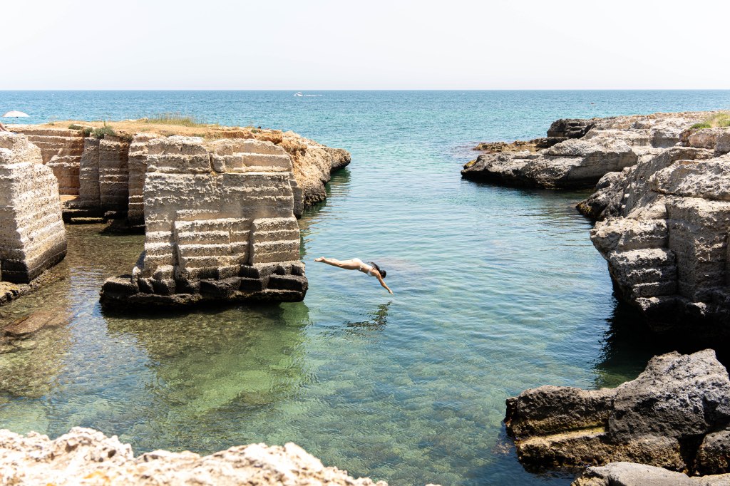 Image of Bianca diving into the crystal-clear waters at Calette Di Torre Cintola, a beautiful beach area in Puglia, Italy, known for its pristine waters and stunning coastal views.