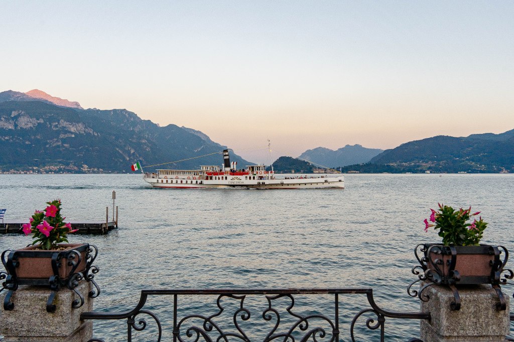 Image of a beautiful sunset at Lake Como, Italy, with the sky ablaze in hues of orange and pink reflecting off the tranquil waters, creating a stunning and serene scene.
