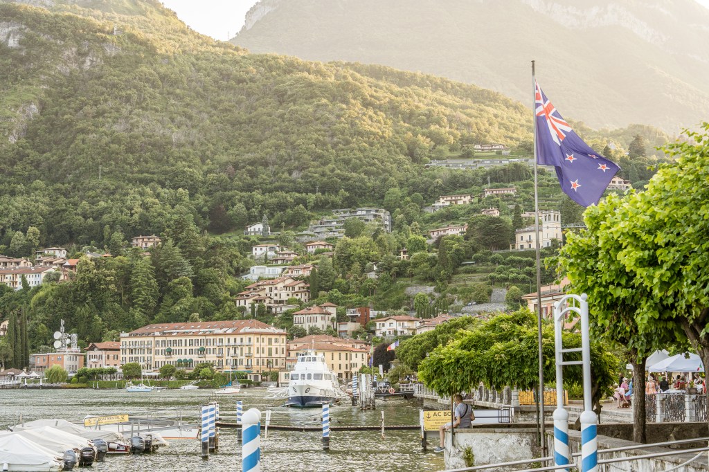 Exciting moment captured as the New Zealand flag flutters in the breeze against the stunning backdrop of Lake Como, Italy, symbolizing a touch of home in a foreign land.