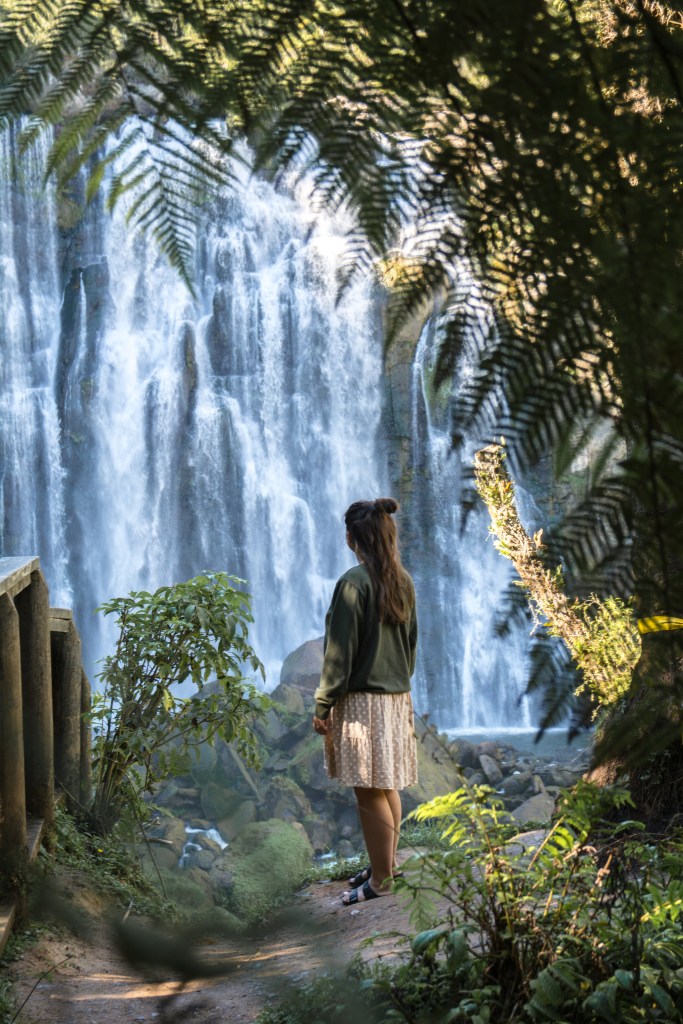 Bianca admiring the breathtaking Marokopa Falls, surrounded by lush greenery. A moment of awe and wonder at one of New Zealand's stunning natural attractions.