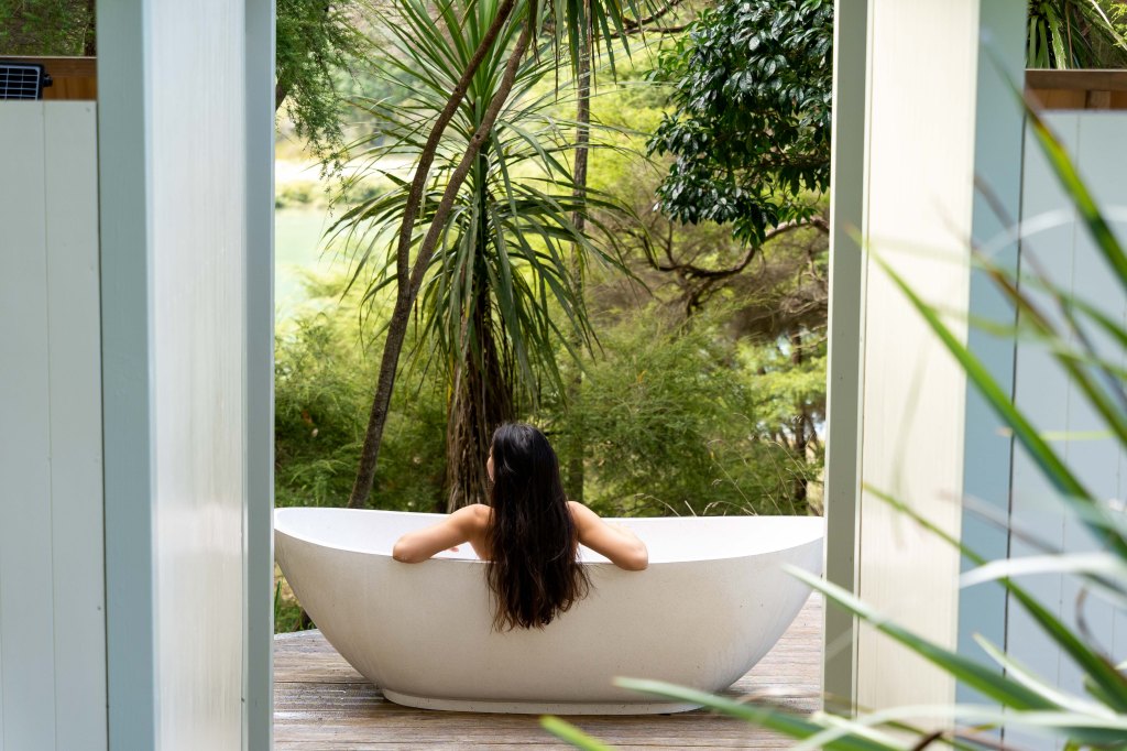 Bianca relaxing in a steaming outdoor bath surrounded by lush New Zealand nature, enjoying a peaceful travel retreat.