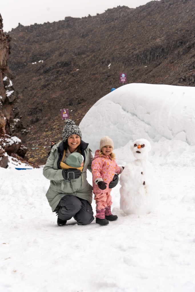 Family building a snowman with kids on Mount Ruapehu during a winter holiday in Tongariro National Park, New Zealand travel blog